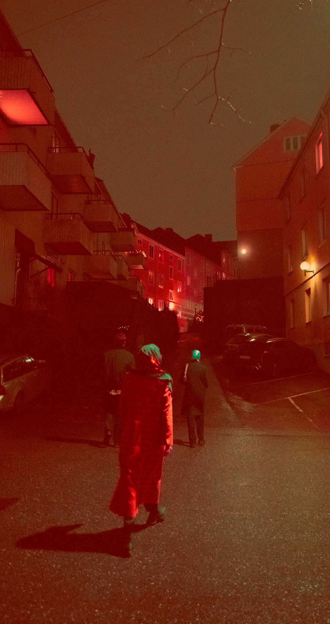 A woman in a long red coat walking up a lamplit street at night